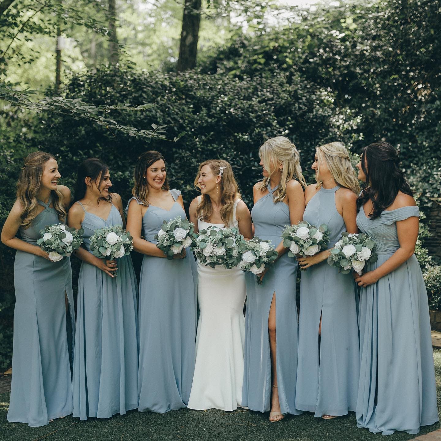 Bride with bridesmaids in dusty blue dresses holding white bouquets