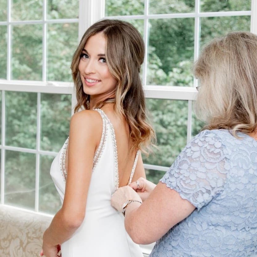 Bride with soft waves having her gown buttoned by her mother